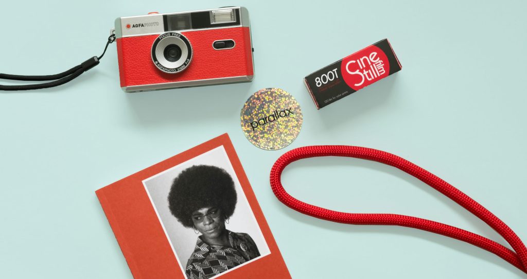 Analogue Photography Gift Guide 2025 - Red Agfa Camera, CineStil 800T film, Red camera strap, Samuel Fosso Photofile book and a sparkly Parallax sticker on a teal background