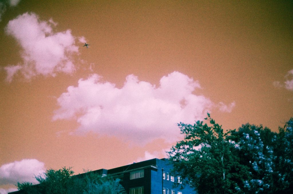 Airplane in an orange sky over a 1930s building and  trees