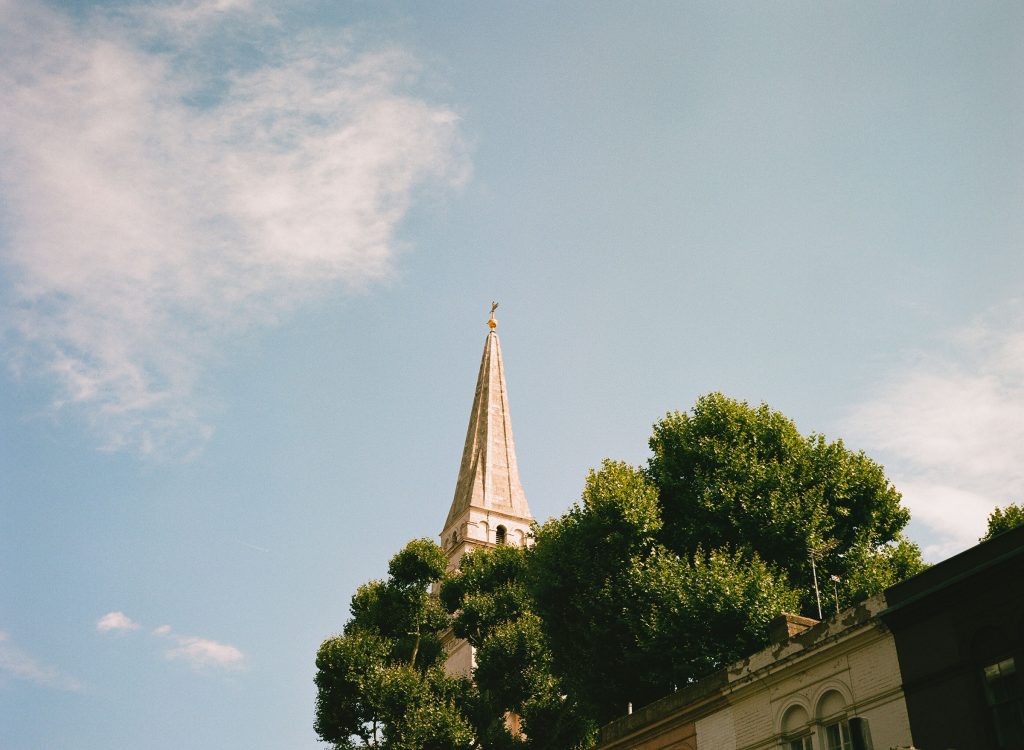 Church spire against blue sky with a tree, Lucky 200 film